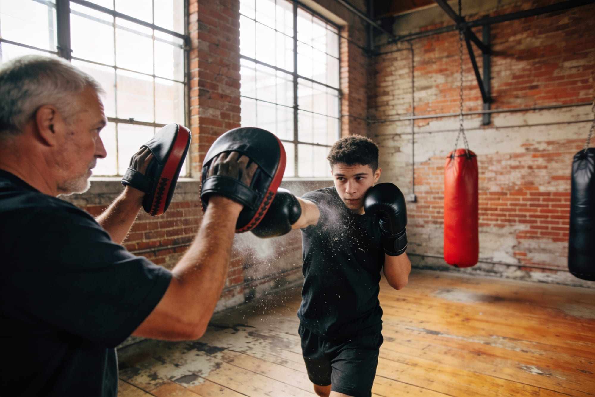 A coach holding focus pads up while a boxer throws a cross